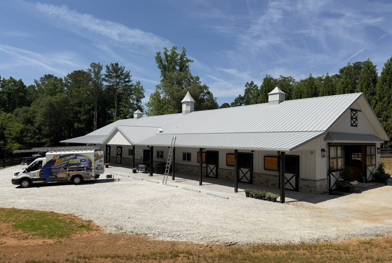 White horse stable with a cupola and fenced paddocks fitted with lightning protection
